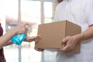 Delivery man wear a white shirt hold cardboard box delivery Parcel post with women use Alcohol gel in home  background Service quarantine pandemic virus concept photo