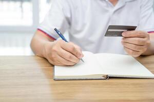 un hombre utilizar lápiz tomar Nota de el uso de crédito tarjeta muy día en planificación dinero gasto foto