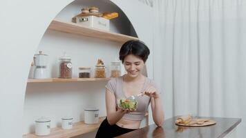 un asiatico giovane donna nel abbigliamento sportivo mangiare verdure insalata nel cucina a casa , salutare stile di vita concetto video