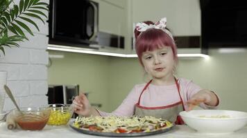 cocinando. pequeño niño en delantal agregando rallado queso a crudo Pizza en cocina video