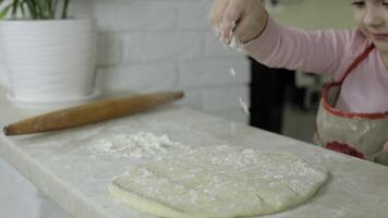 Koken pizza. weinig kind in schort bestrooi de deeg met meel in keuken video