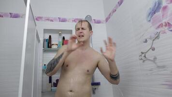 Young handsome fat man takes a shower at bathroom. Emotionally sings and dances video