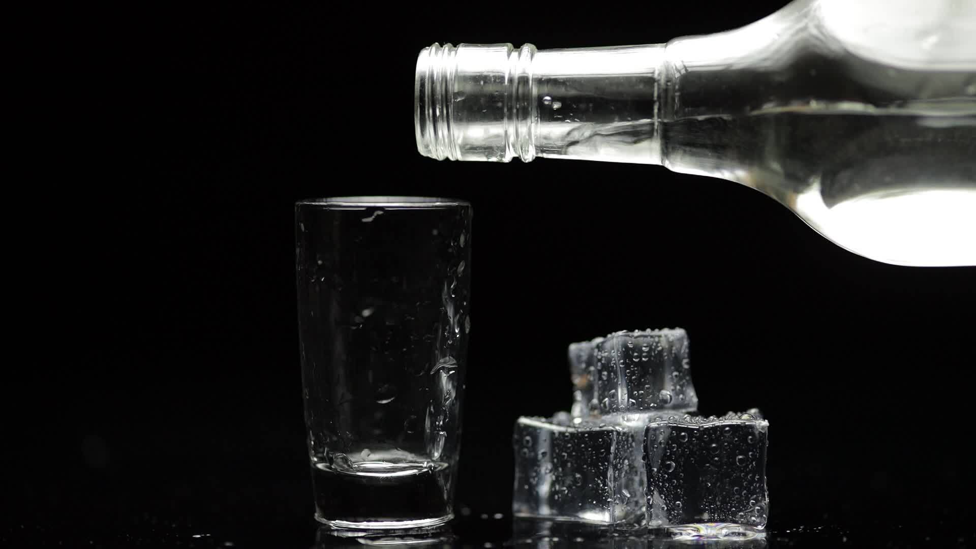 Pouring up shot of vodka into glass. Black background. Pour of alcohol