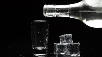 Pouring up shot of vodka into glass. Black background. Pour of alcohol drink video