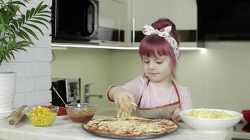 Cooking pizza. Little child in apron adding grated cheese to dough in kitchen video