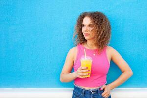 beautiful woman holds delicious orange juice, cold refreshing summer drink. Blue background, isolated. Outdoors, walk around city. portrait. photo