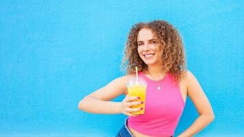 hermosa mujer sostiene delicioso naranja jugo, frío refrescante verano beber. azul fondo, aislado. al aire libre, caminar alrededor ciudad. sonriente. foto