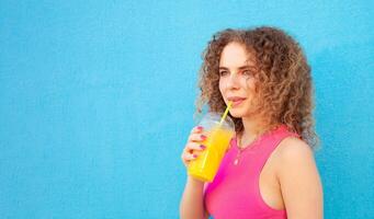 hermosa mujer sostiene delicioso naranja jugo, frío refrescante verano beber. azul fondo, aislado. al aire libre, caminar alrededor ciudad. bebidas foto