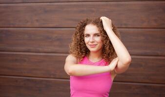 beautiful curly woman in city, against backdrop of brown wall, copy space for text. cheerful, smiling. face. photo