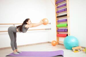 joven mujer es haciendo gimnasia en gimnasia. sano estilo de vida. púrpura estera pelota foto