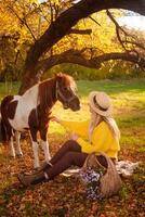 mujer y manchado marrón poni a puesta de sol en bosque, hermosa niña en otoño ropa ama su caballo, concepto de amabilidad, animal cuidado, naturaleza y amistad. sin rostro. foto