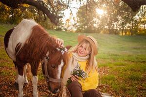 Beautiful portrait, woman and pony, spotted horse, in autumn forest, pleasant colors, background. concept of love, tenderness, friendship. wreath of flowers. photo