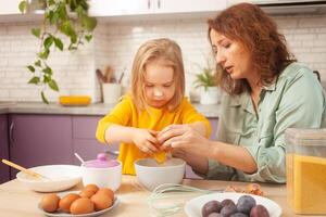 Grandmother and granddaughter cook in kitchen in middle, family pastime, leisure. woman and child make cake in purple, lavender kitchen. plum pie. photo