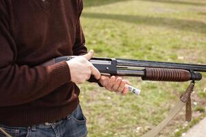 A man charges a pump-action shotgun with a Ammo. 12 caliber. Tyre outdoor. A man in headphones and goggles is preparing to shoot. Firearms for sports shooting, hobby. close up photo