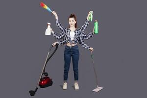 A girl on a gray background in the studio. isolate. A woman with six hands, house. Vacuum, mop, detergent, dust collector, brush, rag. Robot machine for cleanliness. Cleaning company. Fast photo