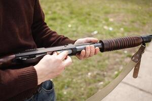 A man charges a pump-action shotgun with a Ammo. 12 caliber. Tyre outdoor. A man in headphones and goggles is preparing to shoot. Firearms for sports shooting, hobby. photo