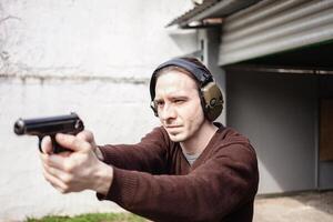 A man is aiming for a gun. A man wearing protective headphones. outdoor tyre shooting range. hobby. firearm against the white wall photo