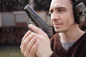 A man shoots a gun, aiming at the target. A man wearing protective headphones. A wall and a roof with bullet holes. outdoor shooting range copy space photo