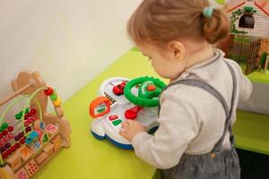 A small two-year-old girl plays with toys in the playroom photo