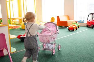 A small two-year-old girl plays with toys in the playroom photo