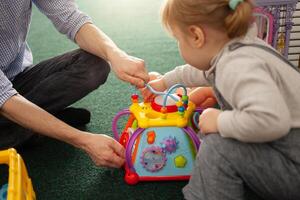 A small two-year-old girl plays with toys in the playroom photo