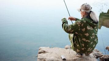 el mayor en banco de río, un hombre con un pescar varilla pesca, hermosa naturaleza, otoño. un antiguo hombre descansa y ama su pasatiempo. activo sano estilo de vida, exterior. elimina el nudo desde el pescar línea foto