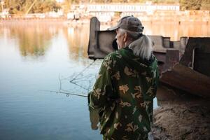 más viejo hombre es pescar en el río. sucio agua, contaminación, basura, oxidado barcazas. ecológico catástrofe, producción desperdiciar. foto