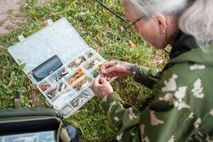 Fishing gear in organizer, box. Various baits for predatory fish. Artificial fish for hook. Weights. Fishing hobbies, outdoor. elderly man photo