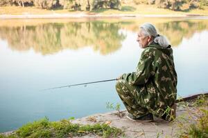 senior concept. pensioner fishes on the river in his spare time. A useful hobby, outdoor activities in old age. copy space. Sits photo