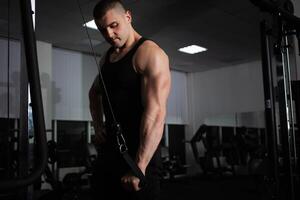 un Deportes atleta entrenador un muscular hombre lo hace un ejercicio en un simulador en gimnasia. retrato, bajo llave, oscuridad. elegante foto