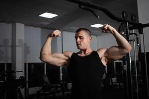 Portrait of an athlete, a sports man coach does an exercise on simulator in the gym. Healthy active lifestyle, shakes muscles. large muscular arms, biceps and triceps photo