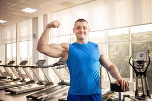 A young handsome coach with a muscular body poses in gym. Bodybuilder, sports physical therapy, weight loss. Sport is a cool, healthy active lifestyle. Indoor concept. portrait photo