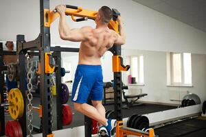 un muscular entrenador en gimnasio es comprometido en Deportes en simuladores. capacitación, entrenamiento, peso pérdida programa. el hombre en simuladores. Copiar espacio, interior concepto, sano activo estilo de vida. Lagartijas foto