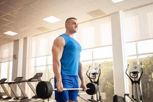 A young handsome coach with a muscular body poses in gym. Bodybuilder, sports physical therapy, weight loss. Sport is a cool, healthy active lifestyle. Indoor concept. rod photo