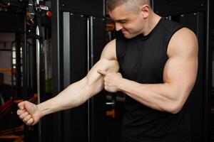 young handsome coach in a black uniform against background of a simulator in gym. Muscular athletic body of a bodybuilder, coaching, individual sports and weight loss courses. Portrait. anatomy photo