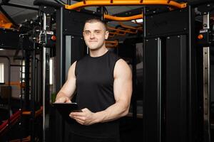 young handsome coach with a tablet in his hands. Coaching, individual courses of sports and weight loss. Modern technology, records the results, social network, Internet. Smiling photo