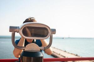 man looks through stationary binoculars. Binoscope on observation deck near sea. seaport in Odessa. Expensive yachts on the pier. Commercial machine, vending business. tourist travels photo