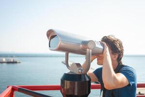 man looks through stationary binoculars. Binoscope on observation deck near sea. seaport in Odessa. Expensive yachts on the pier. Commercial machine, vending business. sky photo