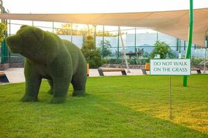 Beautiful bear sculpture of grass, artificial animal, garden decoration. Sign Don't walk on the grass. Sunset photo