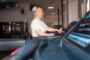 eldest woman of retirement age runs on a treadmill in the gym. Happy, smiling, portrait. Active, athletic, healthy lifestyle in old age. Concept senior. Modern technologies. indoors photo