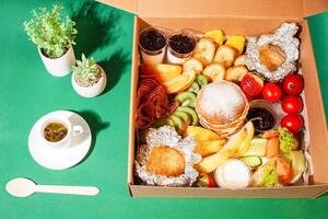 Breakfast in a home delivery box. Beautiful food, tea, green flower plants. Hard shadows, sunlight. Catering photo