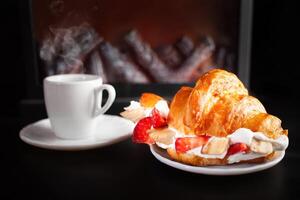 Minimalism, food on a background. Empty text space, mocap. fireplace, tea and croissant with strawberry cream and banana. A cozy warm atmosphere, breakfast dinner lunch. photo