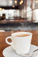 Coffee in a cafe on a wooden table. Drink with steam, smoke. Beautiful blurry background with sideways. Sunlight, interior. Delicious Hot Americano photo