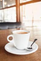 Coffee in a cafe on a wooden table. Drink with steam, smoke. Beautiful blurry background with sideways. Sunlight, interior. Delicious Hot Americano photo