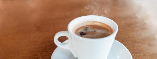 Coffee in a cafe on a wooden table. Drink with steam, smoke. Beautiful blurry background with sideways. Sunlight, interior. Delicious Hot Americano Banner photo