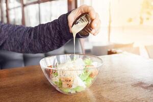 Delicious salad with croutons, grilled chicken breast, grated parmesan cheese and cos lettuce in the gravy boat, simply and healthy recipe, horizontal top view A man pours sauce photo