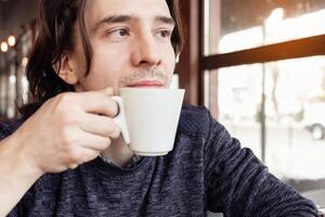 A man drinks coffee in a cafe, a restaurant. interior, natural sunlight, blurred background, sideways. Snack, breakfast. Lunch break. photo