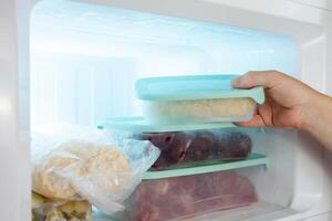 A man pulls frozen vegetables out of the freezer. A man takes corn from the fridge. Plastic containers with frozen meat, vegetables and fruits. photo