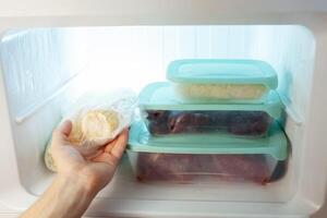 A man pulls frozen vegetables out of the freezer. A man takes corn from the fridge. Plastic containers with frozen meat, vegetables and fruits. photo