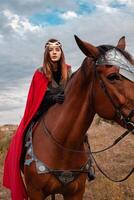 un niña en lado de caballo en contra el cielo. un hermosa mujer en el disfraz de el guerrero reina. foto